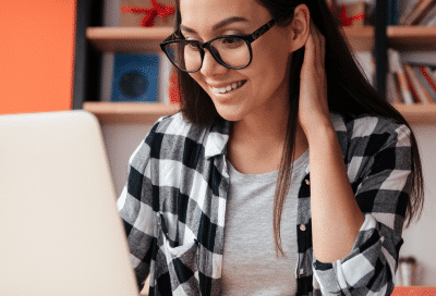 Woman wearing a black and white flannel, smiling while working on a laptop computer, representing Lansdowne Dentistry
