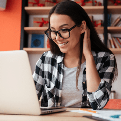 Woman wearing a black and white flannel, smiling while working on a laptop computer, representing Lansdowne Dentistry