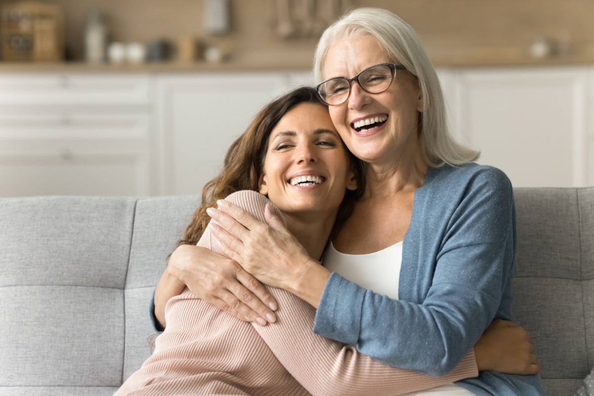 older mother and older daughter hugging on couch