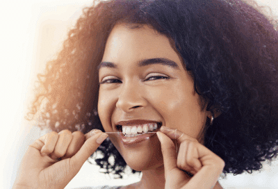 a woman flossing her teeth while smiling, representing the importance of oral health