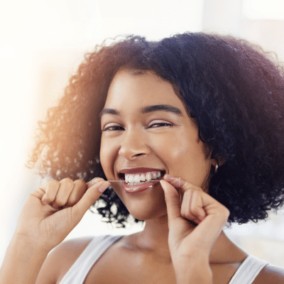 a woman flossing her teeth while smiling, representing the importance of oral health