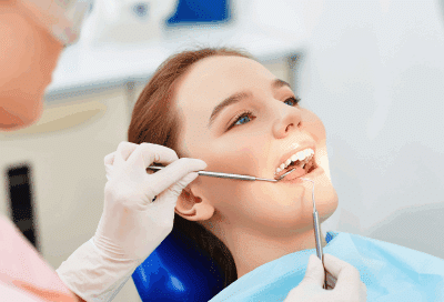 a woman sitting in a dental chair with dentist using tools to work on her teeth, representing regular dental checkups