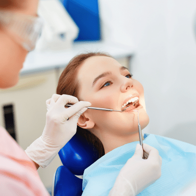 a woman sitting in a dental chair with dentist using tools to work on her teeth, representing regular dental checkups