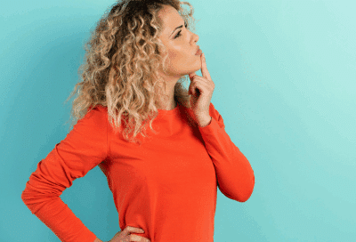 a woman with her finger on her chin, considering which choice to make, representing veneers vs bonding