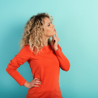 a woman with her finger on her chin, considering which choice to make, representing veneers vs bonding
