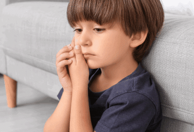 a boy sitting on the floor holding his mouth in pain, representing what to do if your child chips a tooth