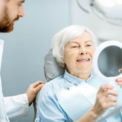 Older woman looking in a small mirror at her new teeth, representing dental implants in lansdowne va
